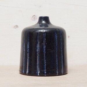 May include: A dark blue ceramic vase with vertical white and blue stripes. The vase has a rounded body and a narrow neck. The stripes add a textured look to the vase.