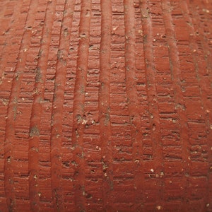 Puede incluir: Primer plano de una maceta de terracota con una superficie texturizada. La maceta es de color marr&oacute;n rojizo y est&aacute; decorada con l&iacute;neas verticales.