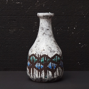 May include: A white ceramic vase with a geometric pattern in brown, blue, and green. The vase has a speckled glaze and a rounded body.