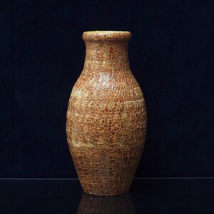 Może przedstawiać: Wazon o fakturze z wąską szyjką i szeroką podstawą. Wazon ma brązowo-beżową kolorystykę z popękanym wzorem na powierzchni. Wazon ma około 25 cm wysokości i prawdopodobnie jest wykonany z ceramiki lub podobnego materiału.