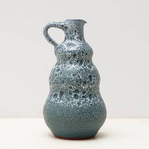 May include: A blue and white ceramic vase with a textured surface. The vase has a wide base and a narrow neck with a handle.