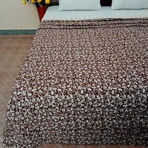 Può includere: Un copriletto con motivo floreale marrone e bianco con due cuscini bianchi su un letto con testiera in legno scuro.