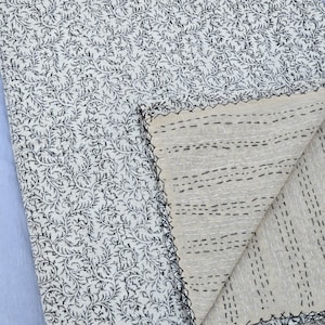 May include: Cream-colored quilt with a black, swirling floral pattern. The reverse side is a solid cream color with horizontal black stitching. The edges are finished with black stitching. This handmade quilt is suitable for a bed or sofa.