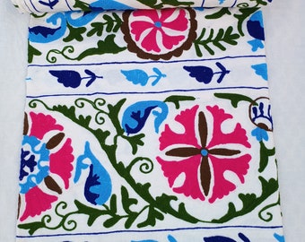 May include: A white fabric textile featuring intricate embroidery in vibrant shades of hot pink, forest green, royal blue, and light blue. The design consists of repeating floral motifs, circular patterns, and swirling vine-like elements.