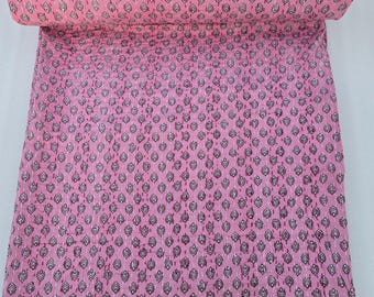 May include: Pink kantha quilt with a white floral pattern. The quilt is folded and rolled up.
