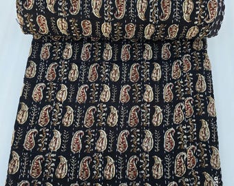 May include: A rolled-up black quilt with a repeating paisley pattern in shades of brown and cream. The quilt is hand-stitched with white thread, and the edges are finished with a white border. The textile is a decorative home good.