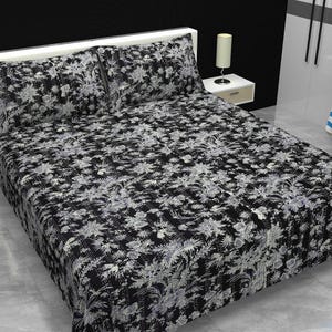May include: A black and white bedspread and two matching pillowcases featuring a dense, intricate floral pattern. The bedding set is displayed on a bed frame, showcasing a consistent monochromatic botanical design across all three textile pieces.