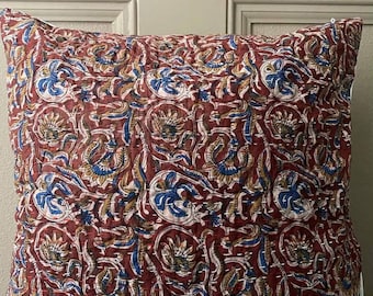 May include: A square throw pillow cover featuring a deep red background with a repeating floral pattern in shades of blue, tan, and white. The fabric is detailed with visible white running stitch embroidery throughout the entire surface.
