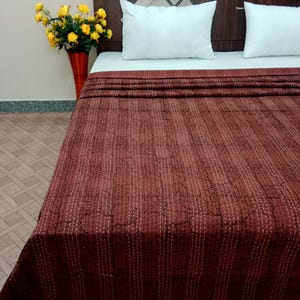 Könnte beinhalten: Eine braune Kantha-Steppdecke mit weißen Nähten, auf einem Bett mit weißen Kissen gefaltet. Die Steppdecke hat ein dezentes Muster und ist aus Baumwolle.