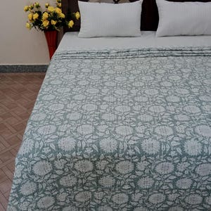Könnte beinhalten: Eine grün-weiße Bettdecke mit floralem Muster, weißem Hintergrund und grünem Blumendesign. Die Bettdecke ist auf einem Bett mit zwei weißen Kissen gefaltet.