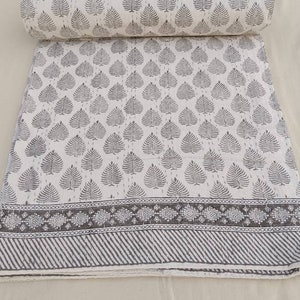 May include: A white cotton fabric with a gray leaf pattern and a gray border. The fabric is rolled up and has a white background.