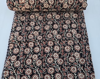 May include: A black and brown floral kantha quilt with a repeating pattern of white flowers and leaves. The quilt is rolled up and has a fringed edge.