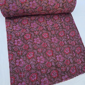 May include: A folded quilt featuring a dark brown base colour with a repeating floral pattern in shades of pink and red. The fabric is detailed with visible white running stitch embroidery throughout, creating a textured kantha style finish.