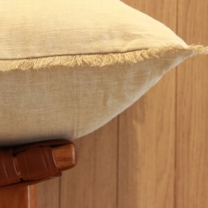 May include: A beige linen pillow with a frayed edge and a brown leather base.