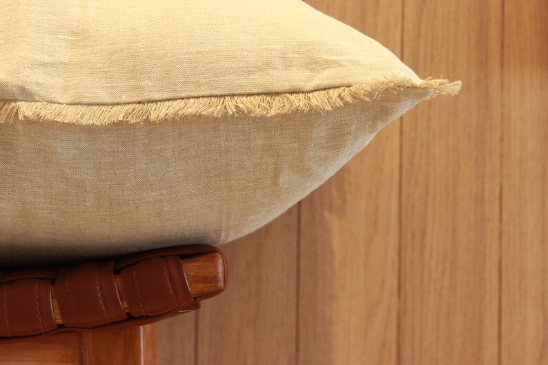 May include: A beige linen pillow with a frayed edge and a brown leather base.