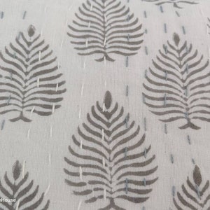 May include: Close-up of a white fabric with a repeating pattern of gray leaf designs. The fabric is stitched with small, white stitches.