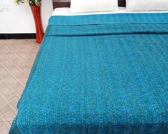 Könnte beinhalten: Eine türkisfarbene Tagesdecke mit einem gesteppten Muster bedeckt ein Bett mit weißen Kissen. Die Tagesdecke hat einen dunklen Rand und ein Blumenmuster. Im Hintergrund steht eine hohe, rote Vase mit gelben Blumen.