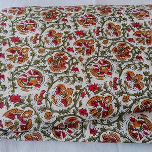 May include: Folded fabric with a repeating floral pattern in red, orange, and green on a cream background. The design features stylized flowers and vines, creating a traditional, decorative look. The fabric appears to be cotton or a similar material.