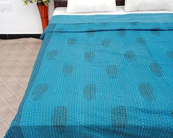 Könnte beinhalten: Eine türkisfarbene Steppdecke mit einem sich wiederholenden Muster aus stilisierten Blattformen und weißen Nähten. Die Steppdecke hat einen gemusterten Rand. Zwei weiße Kissen liegen auf dem Bett, im Hintergrund ein dunkles Holz-Kopfteil.