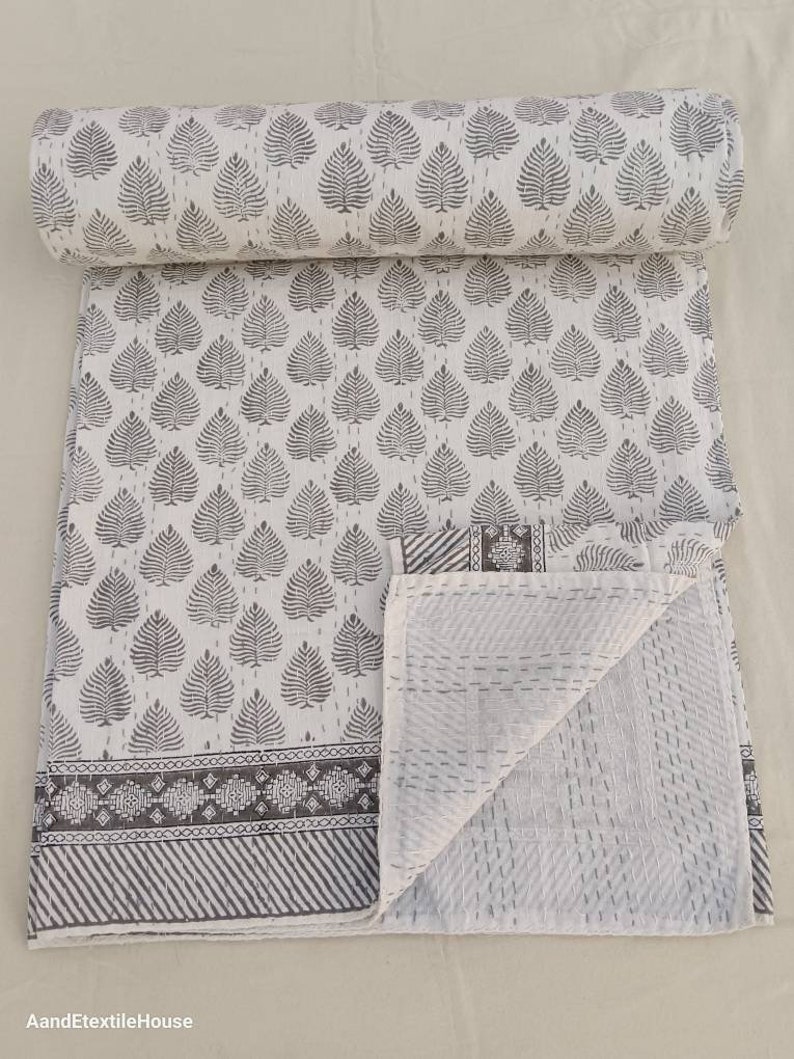 May include: White cotton quilt with a gray leaf pattern and a gray border. The quilt is folded in half and the inside is visible, showing a white cotton fabric with a diamond pattern.