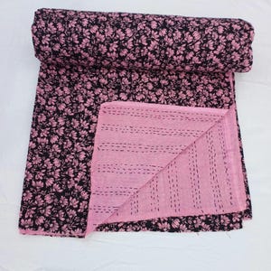 Könnte beinhalten: Eine schwarze und rosafarbene Kantha-Steppdecke mit einem Blumendruck. Die Steppdecke ist in der Hälfte gefaltet und die rosafarbene Seite ist sichtbar. Die Steppdecke ist aus Baumwolle und handgenäht.