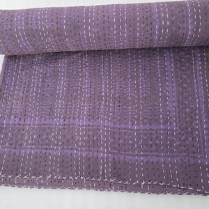Peut inclure: Une courtepointe violette roulée avec un motif floral et des coutures blanches. La courtepointe est faite d'un matériau doux et possède une bordure décorative. C'est un article de décoration intérieure.