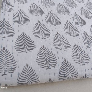 May include: White cotton fabric with a repeating pattern of gray stylized leaves. The fabric is quilted with small stitches.