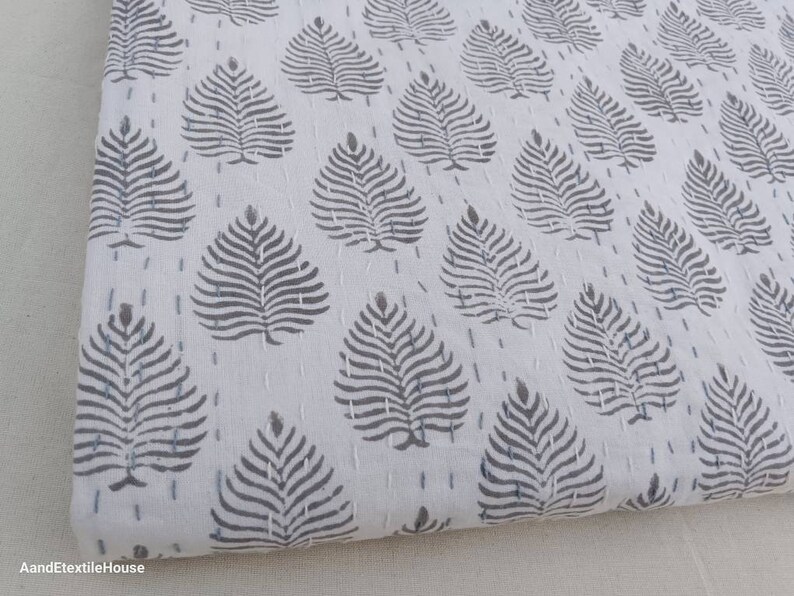 May include: White cotton fabric with a repeating pattern of gray stylized leaves. The fabric is quilted with small stitches.