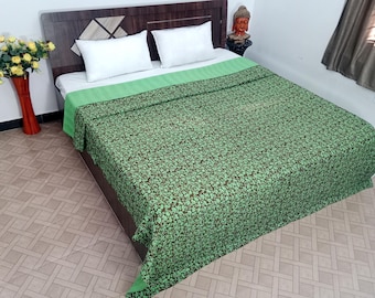 May include: A bed with a green floral patterned blanket and two white pillows. The bed has a dark brown headboard and is set against a light-colored wall. A vase of yellow flowers is on the left.