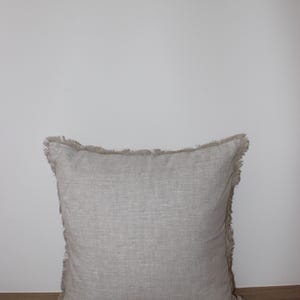 May include: A square, light gray throw pillow with a frayed edge. The pillow is made of a linen fabric and has a subtle texture.