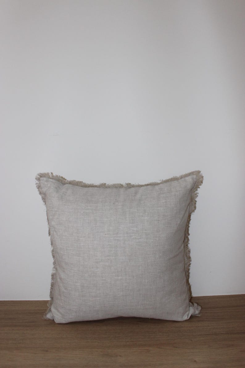 May include: A square, light gray throw pillow with a frayed edge. The pillow is made of a linen fabric and has a subtle texture.