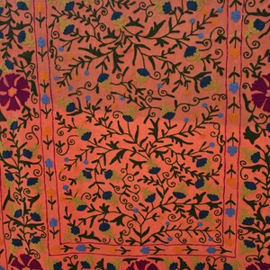 May include: Coral-colored textile with intricate floral embroidery. The design features dark green vines, blue and yellow flowers, and large purple flowers at the corners. The embroidery creates a detailed, textured pattern across the fabric.