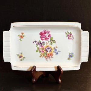 May include: A white rectangular serving tray with a gold rim and a floral design. The design features a pink rose, yellow, purple, and orange flowers, and green leaves.