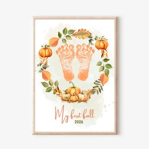 May include: A vertical wall art print featuring a pair of orange baby footprints centred within a circular wreath of watercolour pumpkins and autumn leaves. Below the wreath, the text reads My first fall 2026 in a script and block font.