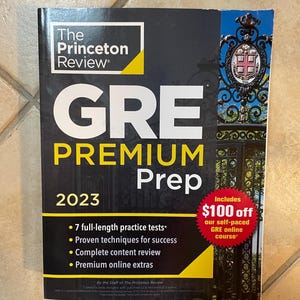 May include: A black and yellow book titled "The Princeton Review GRE Premium Prep 2023" with a red circle that says "Includes $100 off our self-paced GRE online course".