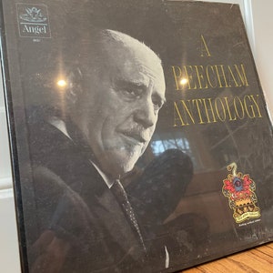 May include: A black and white photo of Sir Thomas Beecham, a British conductor, on the cover of a vinyl record album. The album is titled "A Beecham Anthology" and features the Angel Records logo. The album cover also includes a crest with the words "Nil Sine Labore" (Nothing without labor).