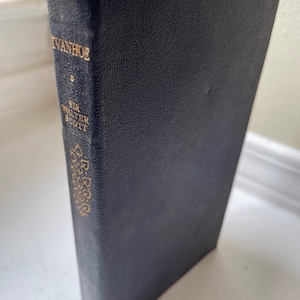 May include: A hardcover book titled "Ivanhoe" by Sir Walter Scott. The book has a dark blue cover with gold lettering and decorative accents. The book's spine displays the title and author's name in gold.