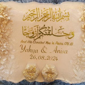 Peut inclure: Un plateau décoratif avec des accents dorés et des fleurs blanches. Le plateau présente de la calligraphie arabe, le texte "And We Created You in Pairs (78.8)", et les noms "Yahya & Anisa" avec la date "26.08.2024".