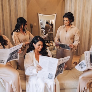 Może przedstawiać: Pięć kobiet w beżowych piżamach czyta egzemplarze gazety "The Wedding Post". Kobieta w środku ma na sobie biały szlafrok.