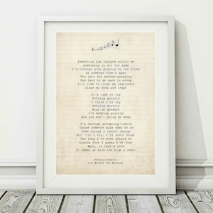 May include: A vintage-style print of the song "Defying Gravity" from the musical Wicked. The lyrics are printed on a cream-coloured background with musical notes at the top. The text is in a typewriter font.