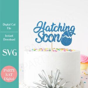 May include: Blue glitter cake topper with the text "Hatching Soon" and a blue glitter egg. The topper is on a white cake with colorful sprinkles.