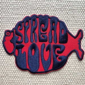 May include: A red fabric patch with a blue embroidered design that says "SPREAD LOVE" in a retro font.