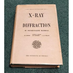 May include: A vintage book titled "X-Ray Diffraction by Polycrystalline Materials" with a light tan cover. The cover features the text "Physics in Industry" at the top, and the Institute of Physics logo. The book is on a green surface.