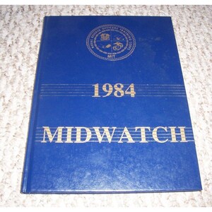 Puede incluir: Un libro de tapa dura azul con letras doradas. El título es "MIDWATCH" y el año es "1984". La portada también presenta un sello con las palabras "Naval Reserve Officers Training Corps MIT".