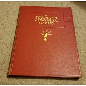 Może przedstawiać: Książka The Scribner Radio Music Library z czerwoną okładką i złotymi napisami. Książka zawiera złotą ilustrację vintage'owego mikrofonu z błyskawicami.