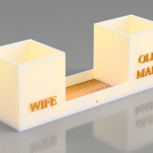 May include: White desk organiser with two compartments. The compartment on the left says "Wife" and the compartment on the right says "Old Man".