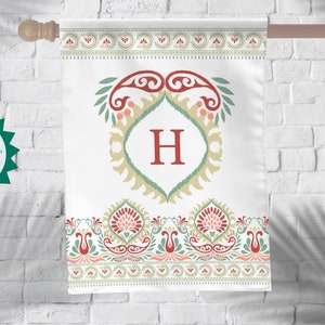 Könnte beinhalten: Eine weiße Gartenflagge mit einem roten, grünen und goldenen Paisley-Muster. Der Buchstabe "H" befindet sich in der Mitte des Designs, umgeben von einem dekorativen Rahmen. Die Flagge ist doppelseitig und hat einen weißen Hintergrund.