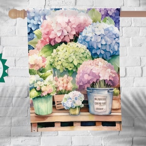 May include: A watercolor painting of a floral arrangement featuring hydrangeas in shades of pink, blue, and green. The flowers are arranged in three buckets, two of which are green and one is blue. The blue bucket has a label that reads "WILDFLOWER FARMING CLUB SINCE 1973".