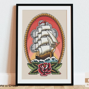 May include: A cross stitch pattern featuring a traditional nautical tattoo design. A white sailing ship with billowing sails is framed by a rope circle and set against a red sunset. A red rose with green leaves is below the ship.