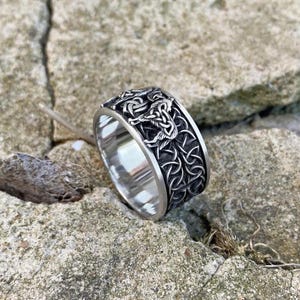 May include: A silver ring with a detailed design of two wolves intertwined. The ring is made of metal and has a polished finish.